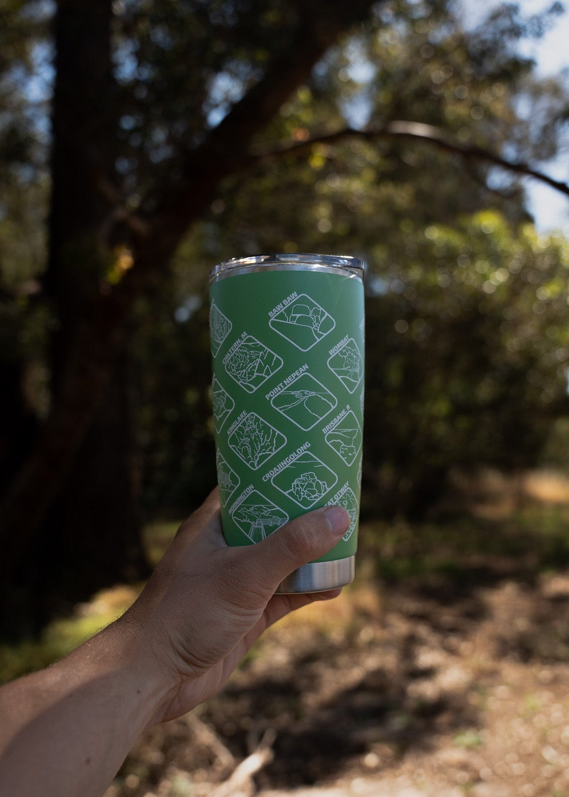 Hand holding a green tumbler with a pattern against a natural background